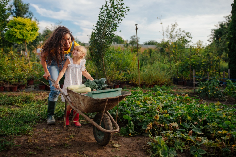 A mother and daughter pushing a wheelbarrow together.