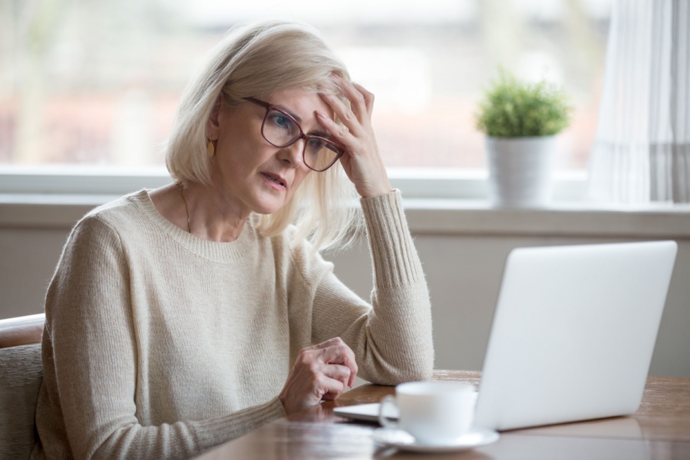 A retired woman looking worried while using a laptop.